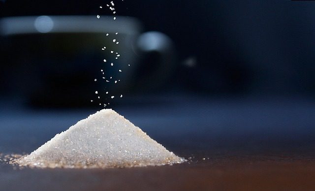 Granulated sugar falling onto a small pile on a surface.
