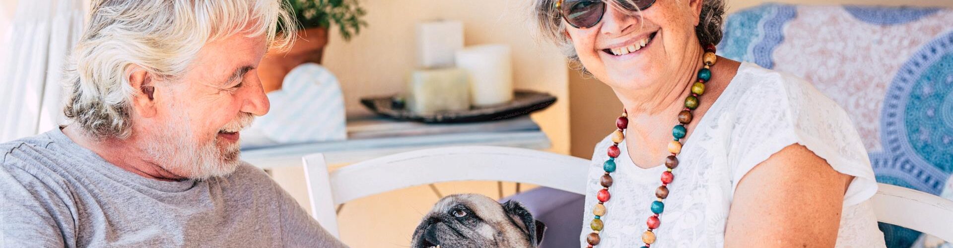 Smiling elderly woman with sunglasses holding a pug dog.