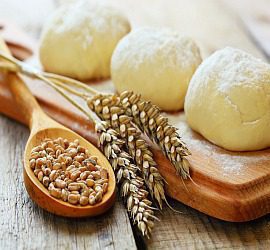 Dough balls and wheat grains with stalks on a wooden board.