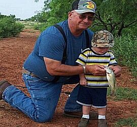 Man and child holding a fish outdoors.