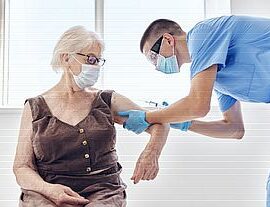Healthcare worker administering vaccine to elderly woman.