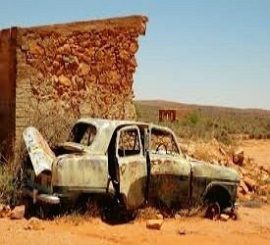 Abandoned rusty car near old stone building.
